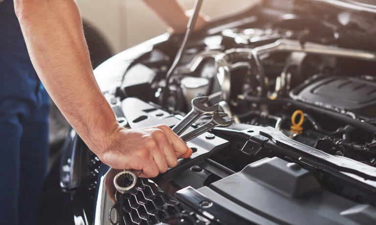 Mechanic with wrenches looking under a car's hood